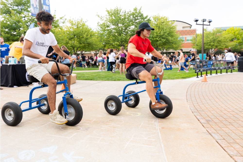 two students riding tricycles during Laker Kickoff race
